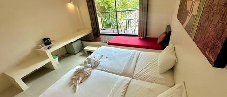 Une chambre d’hôtel avec deux lits, un petit bureau, une fenêtre donnant sur un espace verdoyant et un balcon aménagé avec du mobilier d’extérieur.