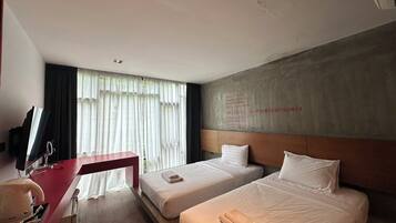 A hotel room with two beds, a desk with a computer, and a large window with curtains.