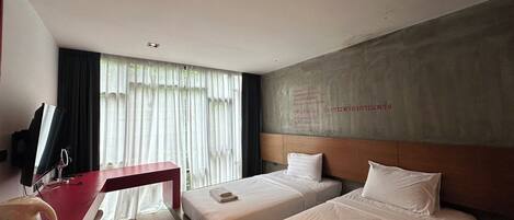 Ein Hotelzimmer mit zwei Betten, einem Schreibtisch mit Computer und einem großen Fenster mit Vorhängen.