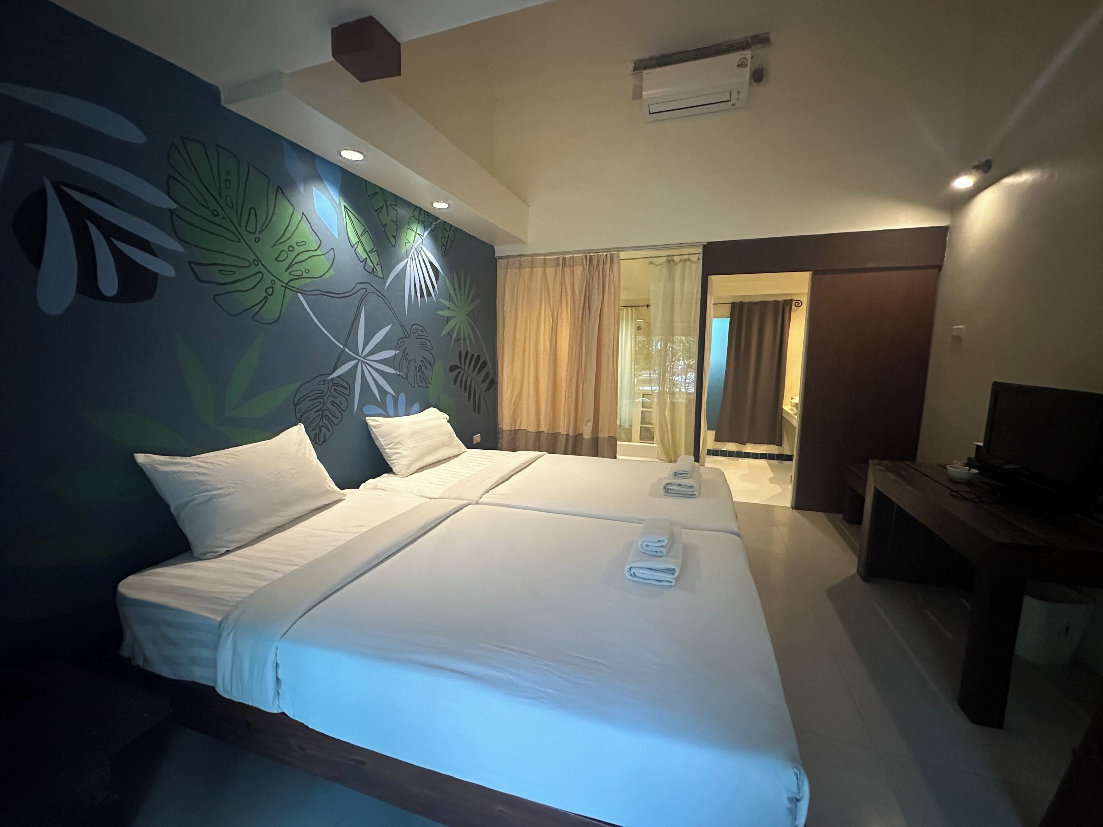A hotel room with a bed, a TV, and a bathroom visible through an open door.