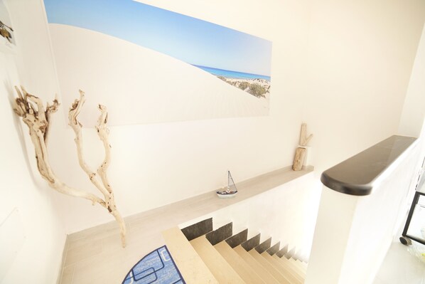 A staircase with a view of the beach, a small decorative item on the landing, and a piece of driftwood on the wall.