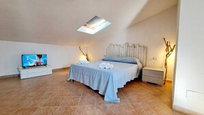 A bedroom with a bed, a TV, a nightstand, and a wall-mounted light. - FollowTheSun- Sea View House (Portoscuso)