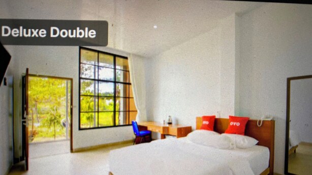 A room with a large bed, a desk, and a chair. There is a window with a view of greenery outside. - OYO 94316 BPG (Banda Aceh)