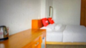 A blurred room with a wooden desk and a bed with white bedding. - OYO 94316 BPG (Banda Aceh)