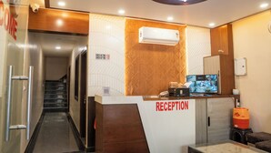Uma área de recepção com balcão, tela digital e ar-condicionado fixado na parede.