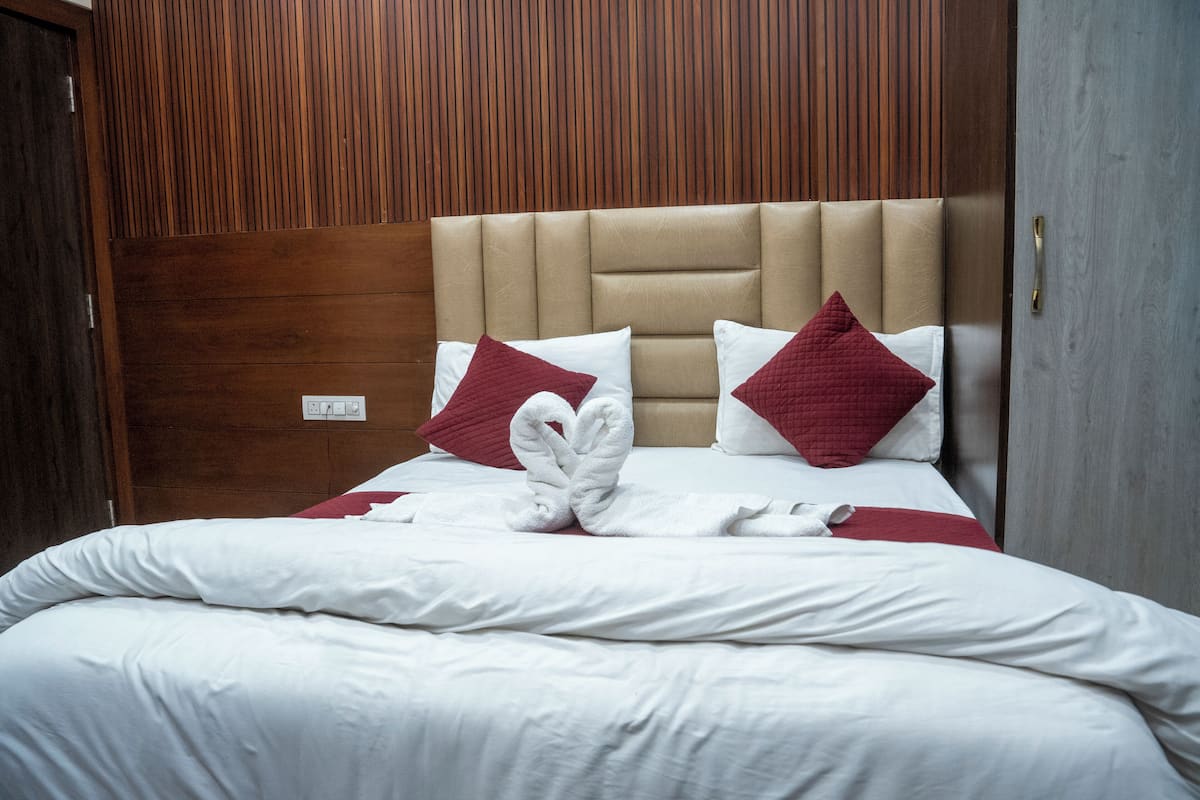 A neatly made bed with white linens and red pillows, a wooden headboard, and a wooden panel wall.