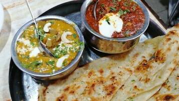 A meal with two bowls of curry and a flatbread on a metal plate.