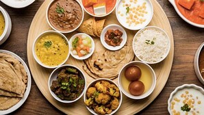 Uma bandeja de madeira com diversos pratos indianos, incluindo arroz, curry e pão.