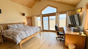 A bedroom with a bed, desk, chair, TV, and a view of the outdoors.