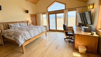 Une chambre à coucher comprenant un lit, un bureau, une chaise, un téléviseur et donnant sur l’extérieur.