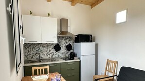 A compact kitchen with a wooden ceiling, a microwave, a refrigerator, and a dining table with chairs. - Anastasia beach cottage Sunflower (Siracusa)