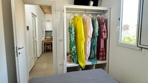 A bedroom with a bed, a wardrobe with hanging clothes, a window, and a TV on the wall. - Anastasia beach cottage Sunflower (Siracusa)