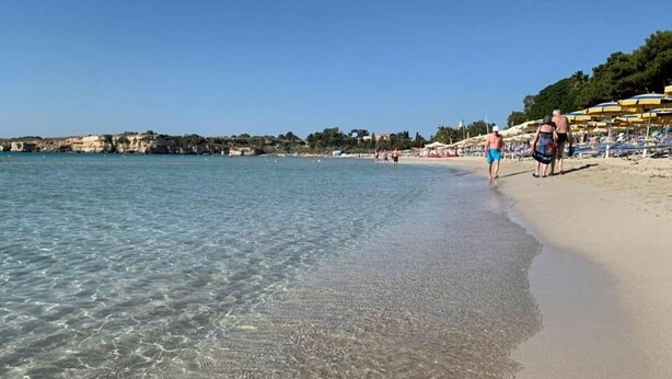 A beach with clear water, people walking, and beach umbrellas. - Anastasia beach cottage Sunflower (Siracusa)