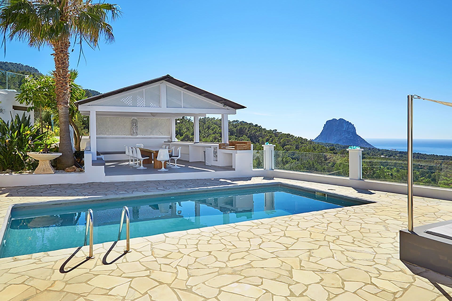A pool area with a patio, seating, and a view of a mountain.
