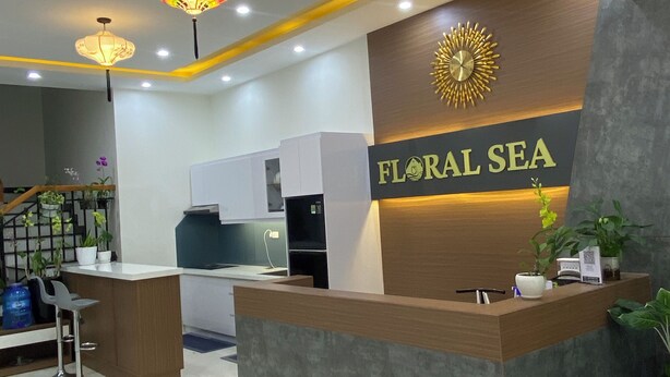 A reception area with a wooden reception desk, a clock, and a sign that reads "FLORAL SEA". - Floral Sea Homestay (Da Nang)
