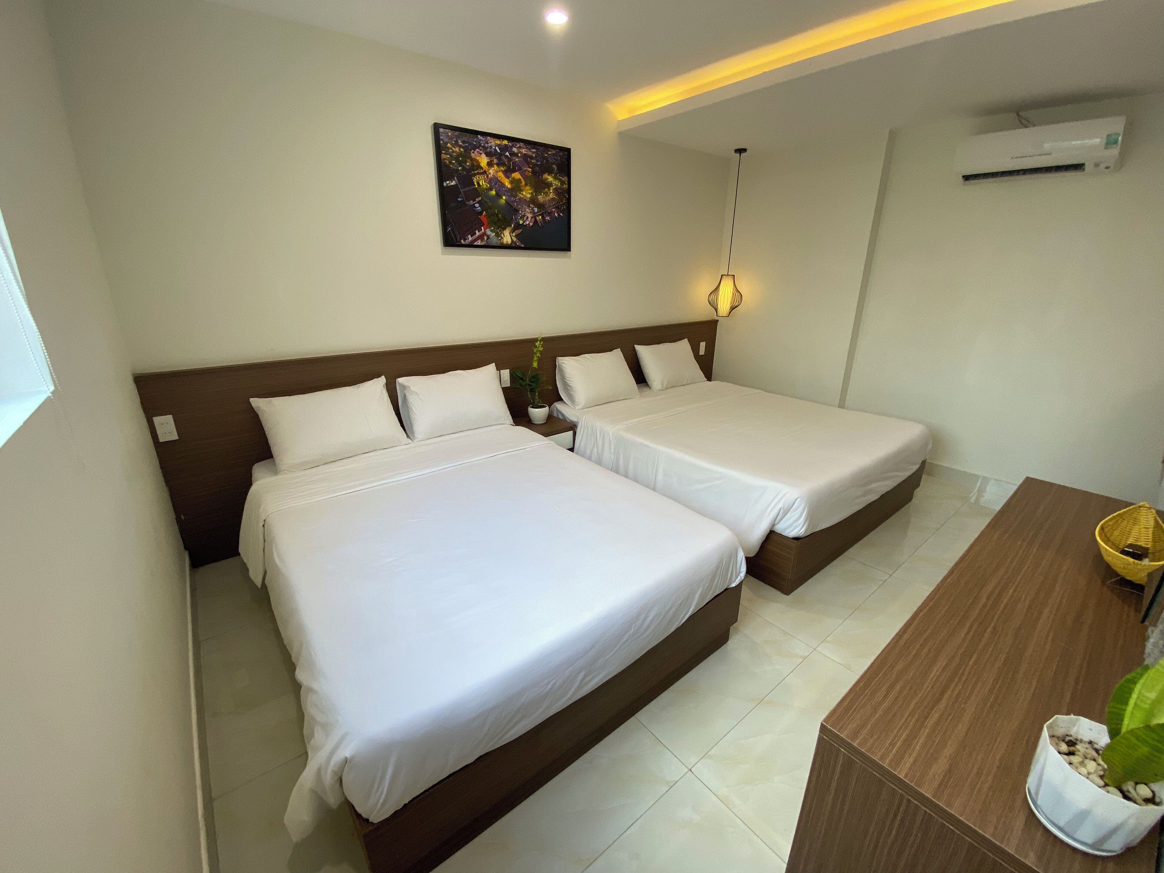 Ein Hotelzimmer mit zwei Betten, einem Nachttisch, einer Topfpflanze und einer Wand-Klimaanlage.
