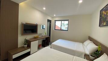 A hotel room with a bed, a desk, a TV, a window, and a plant.