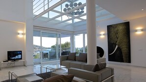 A spacious living area with a large window, a flat-screen TV, a sofa, and a large elephant painting. - My Rental Homes - Villa Bridget with private pool and terraces (San Jose)