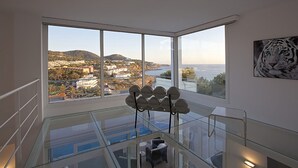 A modern interior with a glass balustrade, a view of a coastal town, and a tiger artwork on the wall. - My Rental Homes - Villa Bridget with private pool and terraces (San Jose)