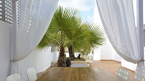 A room with a wooden table, white chairs, a palm tree, and white curtains. - My Rental Homes - Villa Bridget with private pool and terraces (San Jose)
