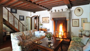 A cozy living room with a fireplace, floral patterned sofas, a wooden coffee table, and a staircase leading to another level. - Elegante villa con piscina a soli 12 km da Firenze ideale per famiglie e gruppi (Toscana)