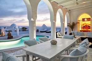 A rooftop pool area with a view of the sea, white furniture, and a Buddha statue.