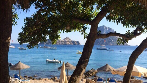 Une plage avec des parasols, des chaises longues et des bateaux sur l’eau.