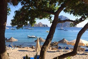 A beach with umbrellas, lounge chairs, and boats in the water.