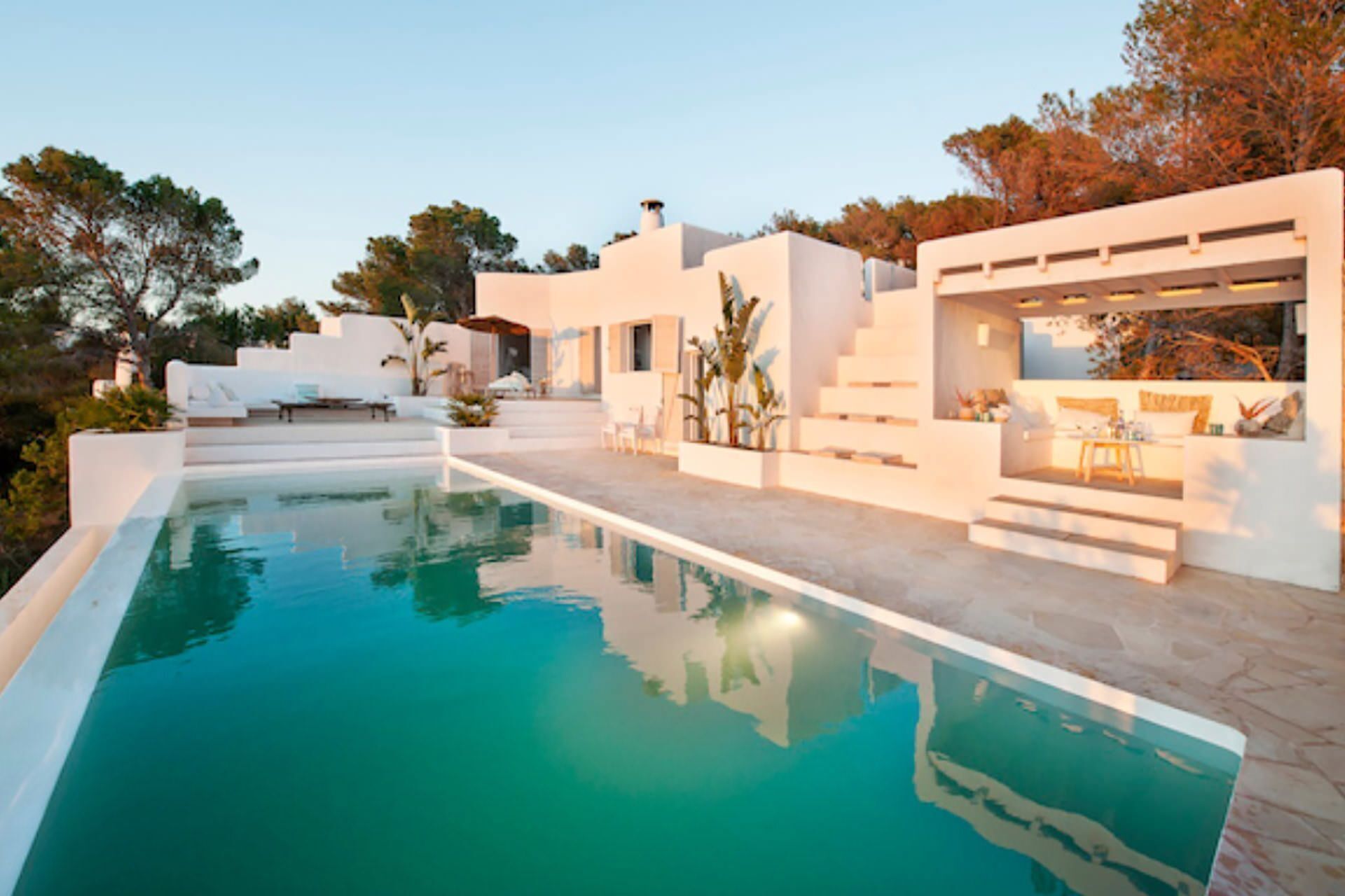 Un área moderna junto a la piscina con una pileta cristalina, arquitectura blanca y escalones que conducen a un espacio de descanso techado.