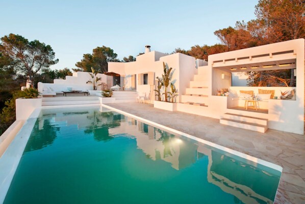 A modern poolside area with a clear pool, white architecture, and steps leading to a covered seating area.