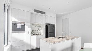 A modern kitchen with white cabinetry, a marble countertop island, stainless steel appliances, and a window providing natural light. - Swainson on Hindmarsh (Adelaide)