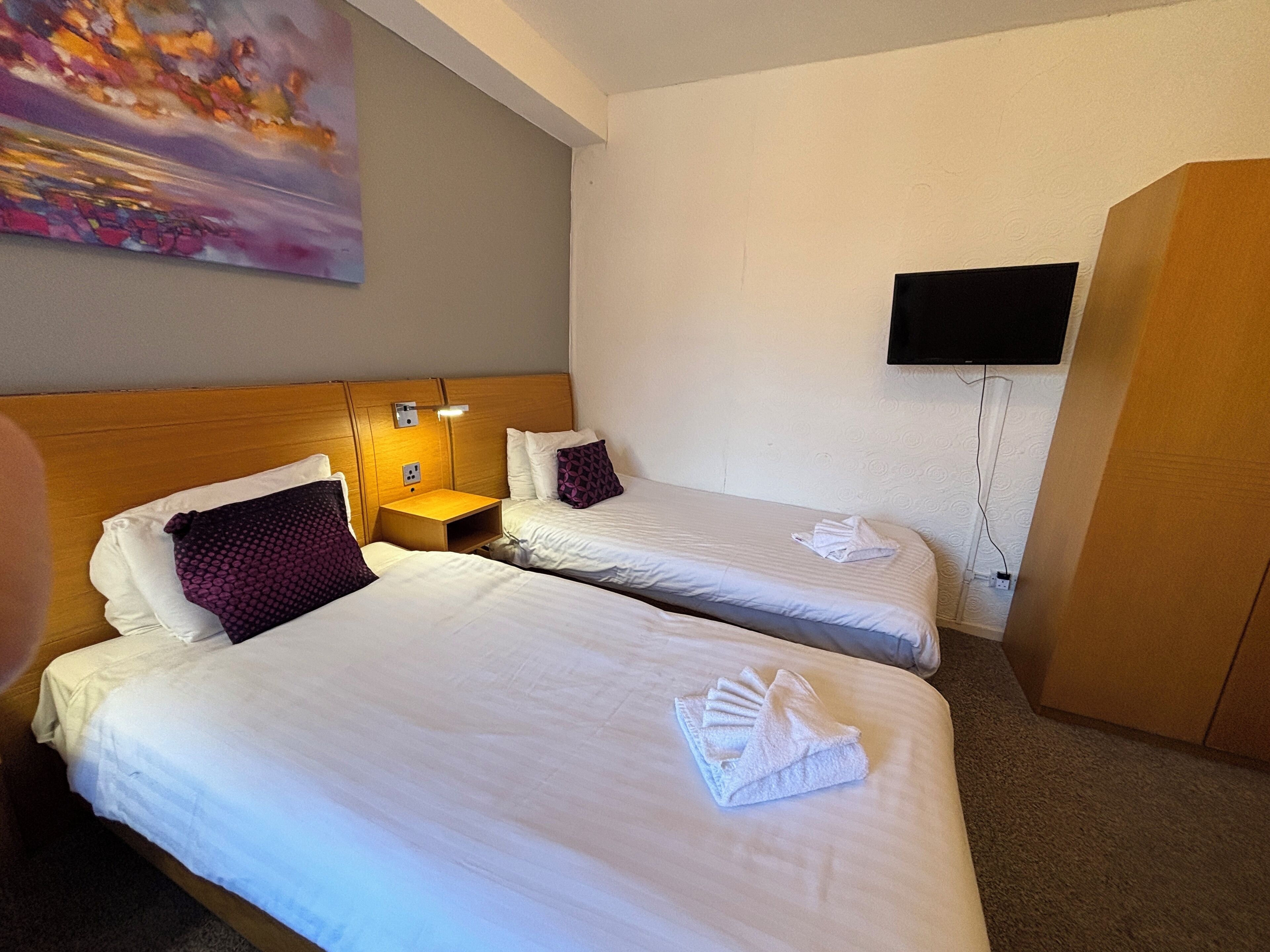 A hotel room with two beds, a TV mounted on the wall, and a painting above the beds.