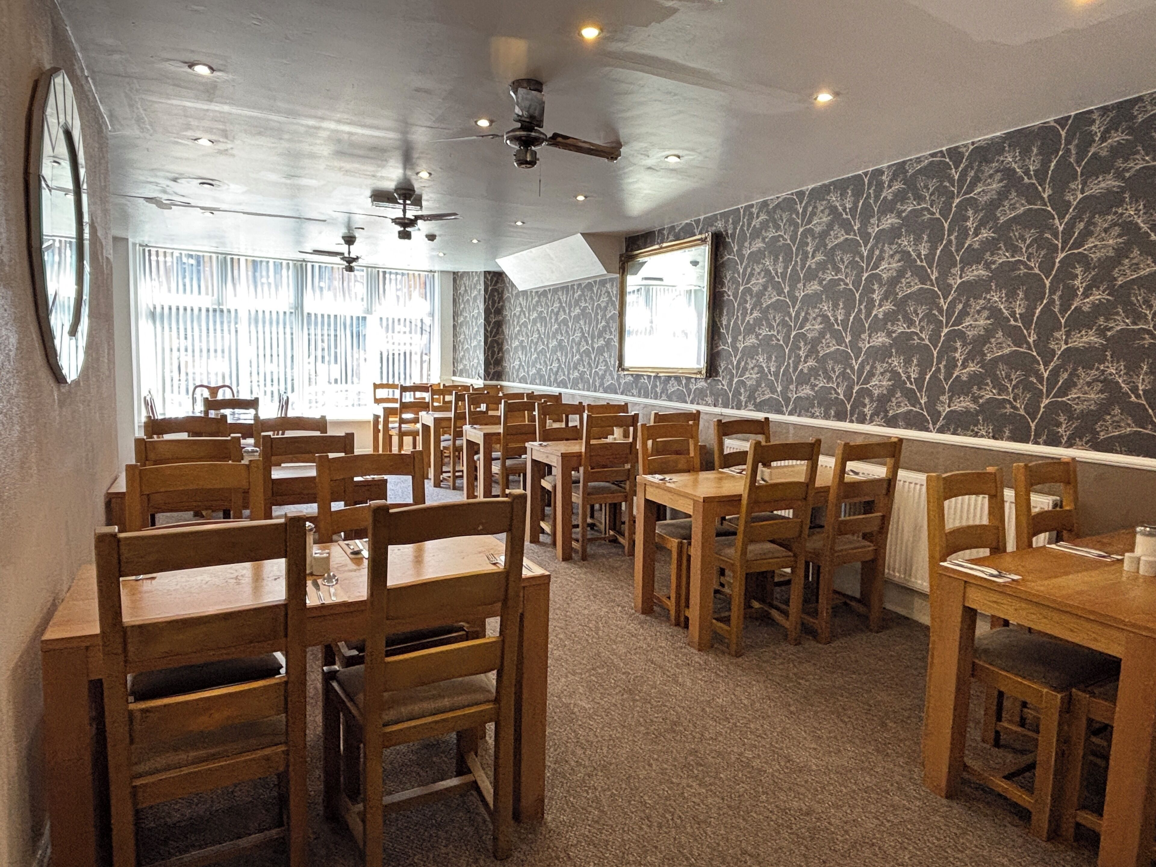 A restaurant with wooden tables and chairs, ceiling fans, and a patterned wall.