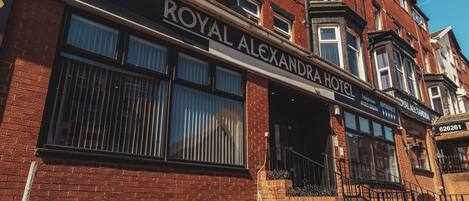 Fachada de hotel con un cartel llamativo que dice "ROYAL ALEXANDRA HOTEL" y una entrada visible.