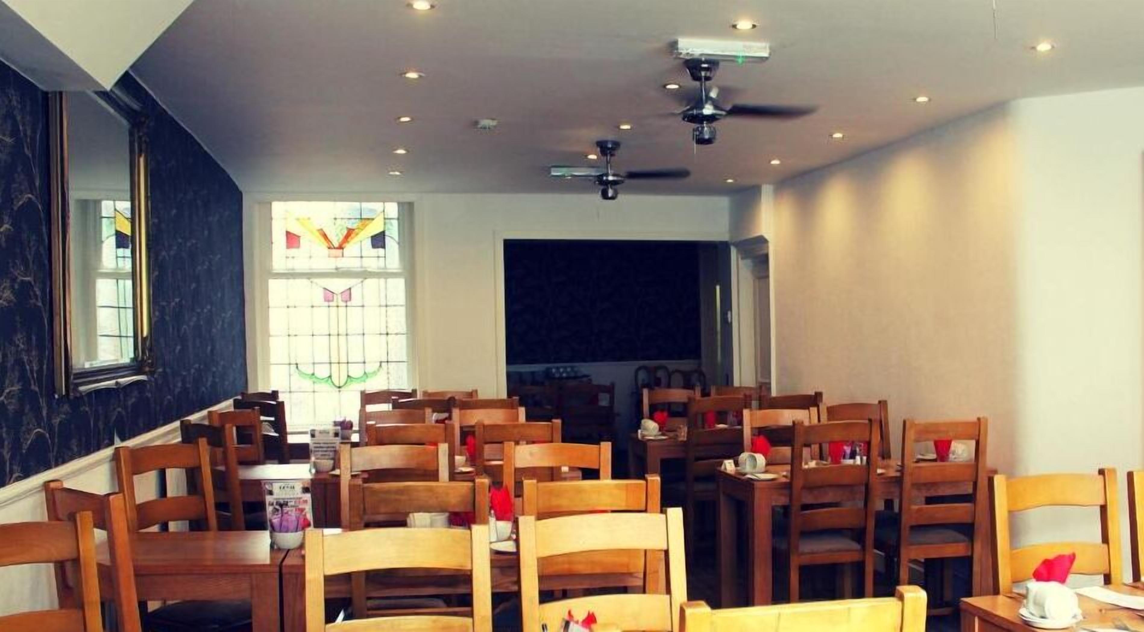 A dining area with wooden tables and chairs, a ceiling fan, and a stained glass window.