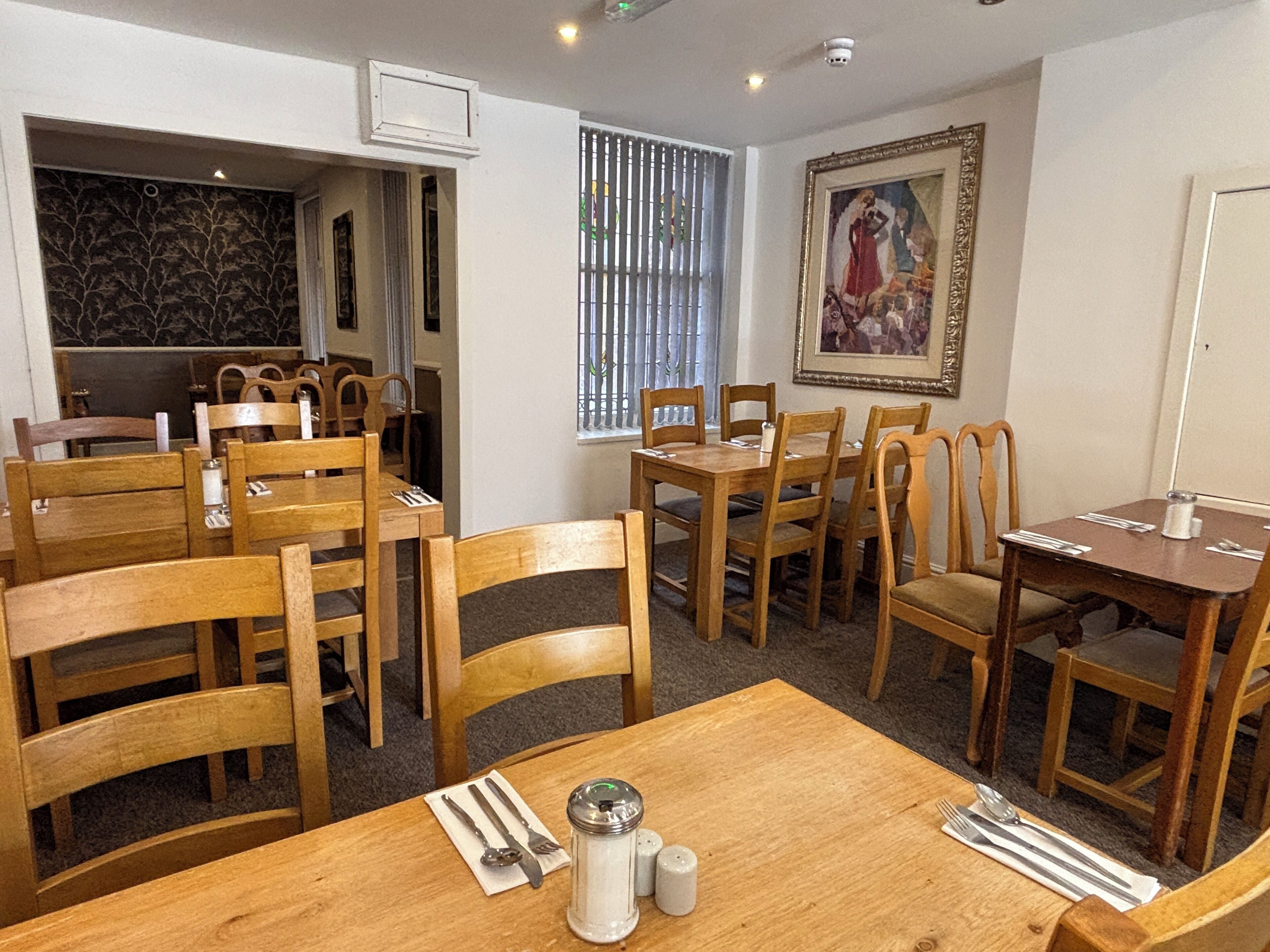A dining area with wooden tables and chairs, a salt and pepper shaker, and a framed painting on the wall.