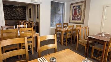 Un coin repas avec des tables et des chaises en bois, un salier et un poivrier, et un tableau encadré accroché au mur.