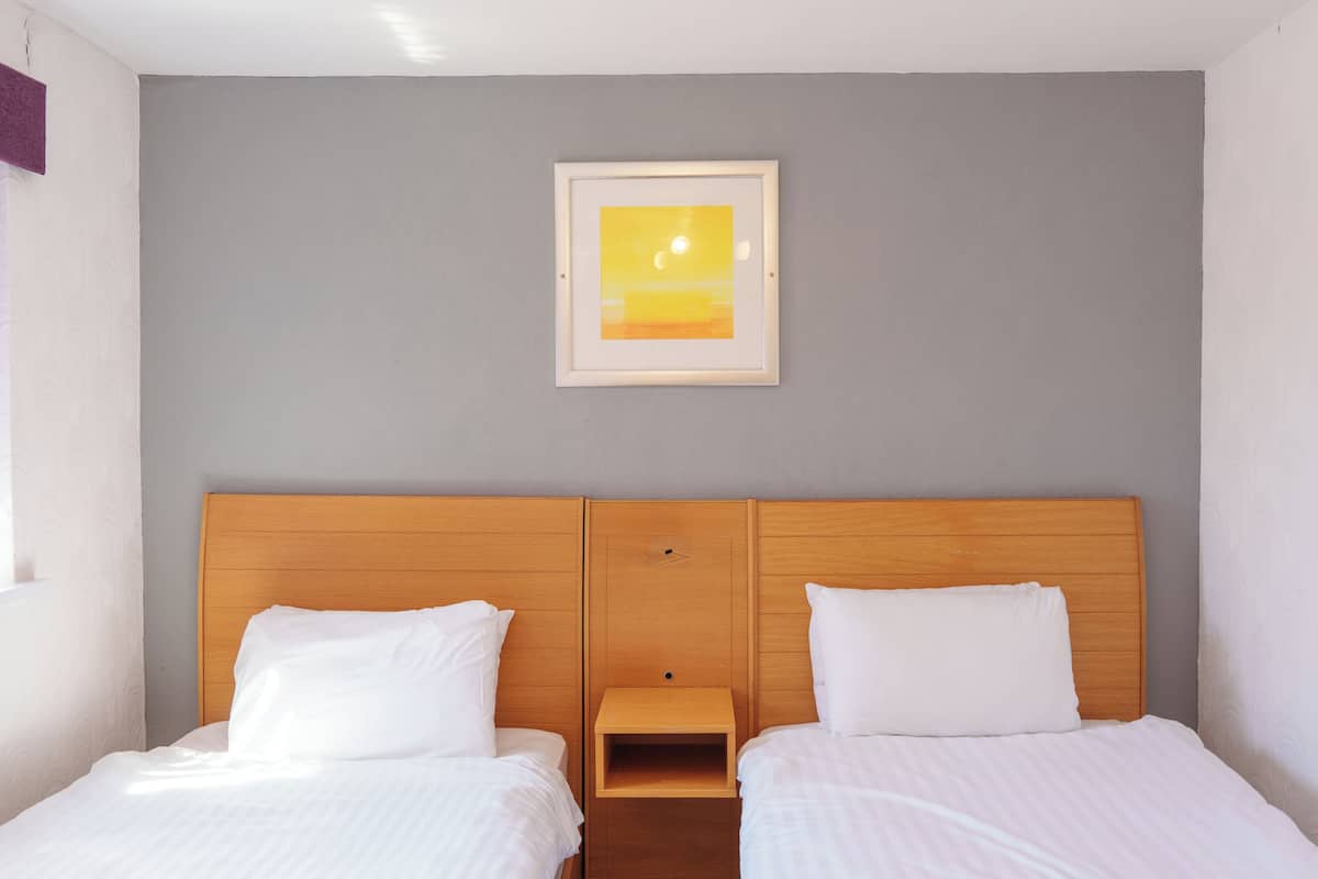 Habitación de hotel con dos camas, cabecera de madera, mesita de noche y un cuadro en la pared.