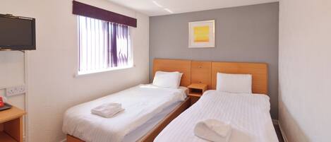 A hotel room with two single beds, a TV, a window with curtains, a painting on the wall, and a wooden nightstand.