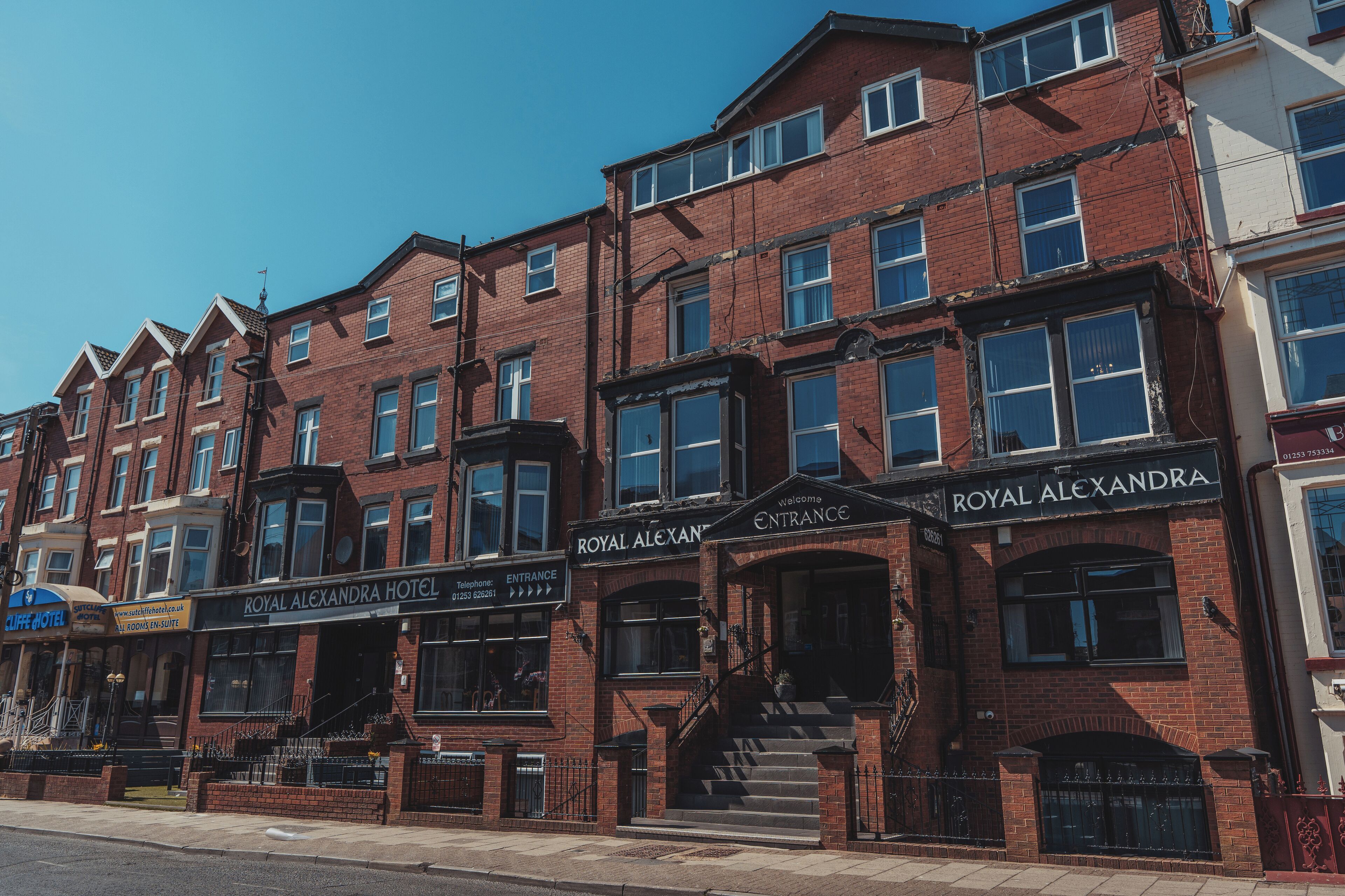 A row of red brick buildings with multiple windows, including a hotel named 'Royal Alexandra Hotel' with an entrance sign.