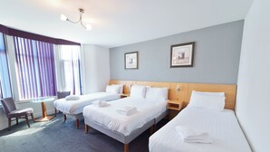A hotel room with three beds, a round table, and a chair. - The Royal Alexandra Hotel by Compass Hospitality (Blackpool)