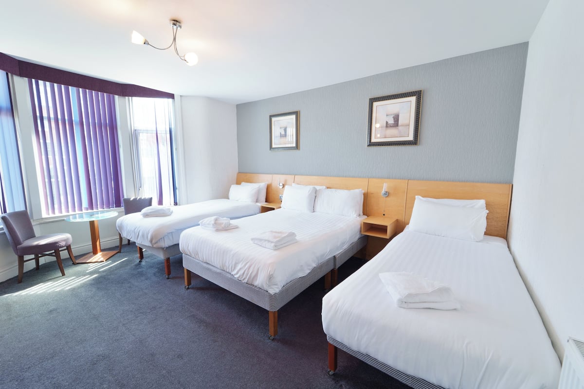 Habitación de hotel con tres camas, una mesa redonda y una silla.