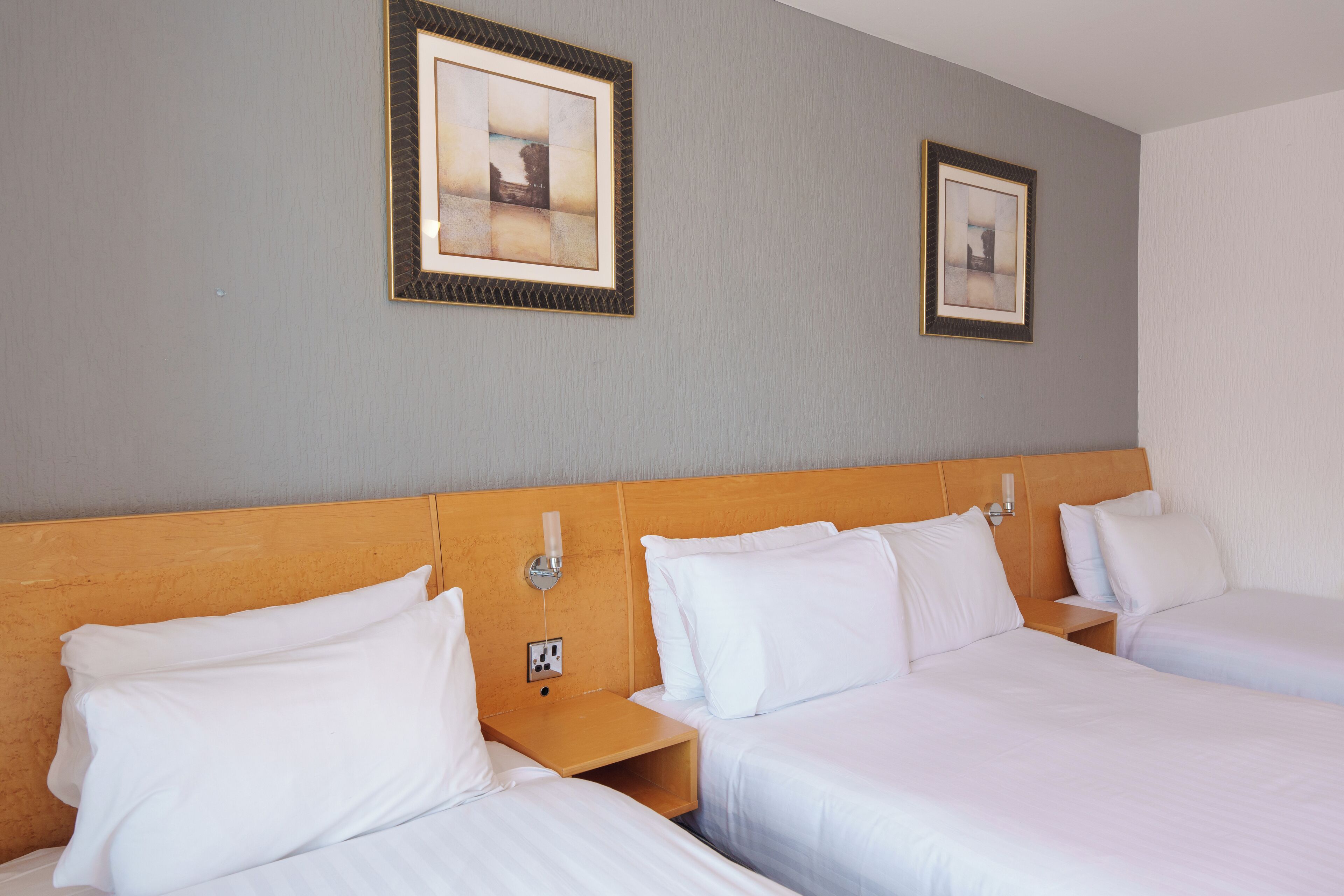 Een hotelkamer met twee eenpersoonsbedden, een houten hoofdbord, een nachtkastje en twee ingelijste foto's aan de muur.