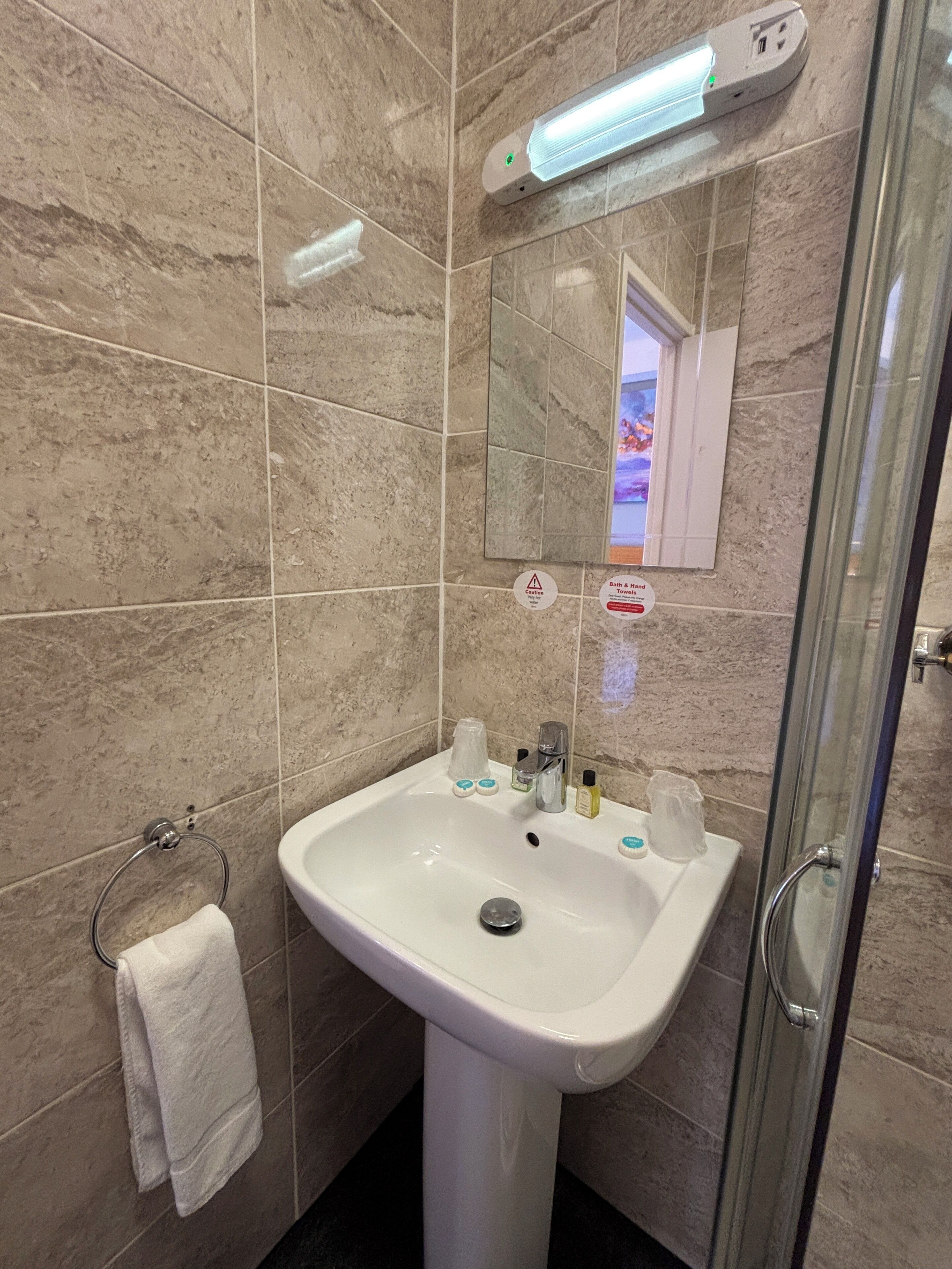 Une salle de bain avec un lavabo blanc, une cabine de douche en verre et un miroir au-dessus du lavabo.