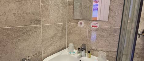 Un baño con lavamanos blanco, cabina de ducha de vidrio y espejo sobre el lavamanos.