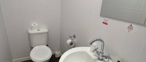 Ein kleines, weißes Badezimmer mit Toilette, Waschbecken und Spiegel.