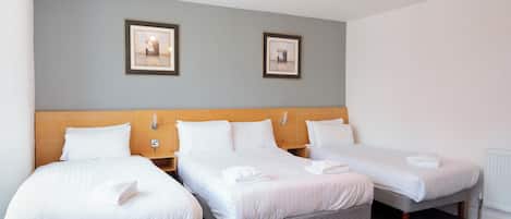 Une chambre d’hôtel avec trois lits simples, une tête de lit en bois et deux tableaux encadrés au mur.