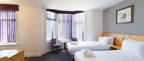Ein Hotelzimmer mit zwei Betten, einem kleinen Tisch, einem Stuhl und einem Schminktisch.