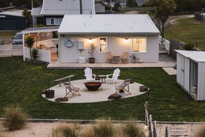 Ein Haus mit überdachter Terrasse, Sitzgelegenheiten im Freien und einem Feuerkorb.