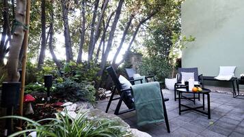 Un espace extérieur aménagé avec des chaises et une table, entouré de verdure et d’arbres.